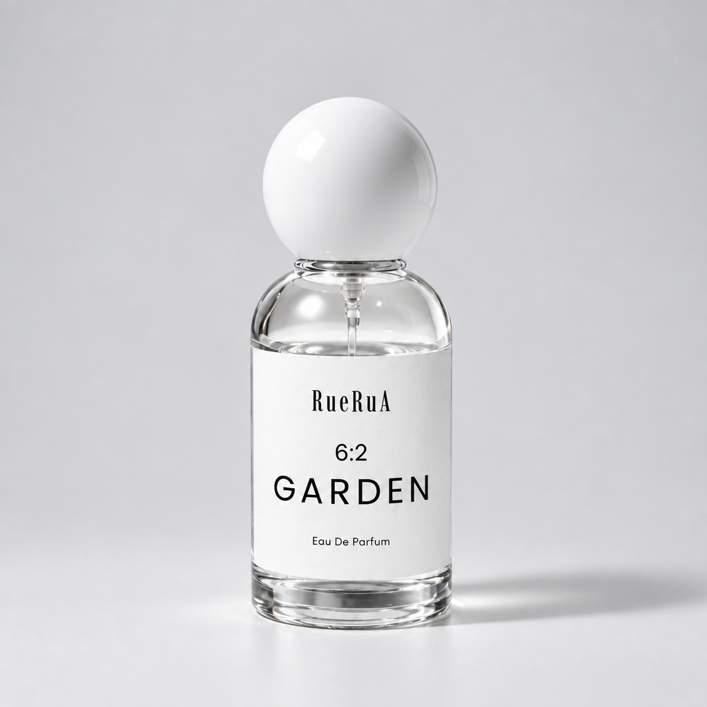 A clear glass perfume bottle with a white spherical cap and a white label reading RueBula 6:2 GARDEN Eau De Parfum, set against a light gray background.